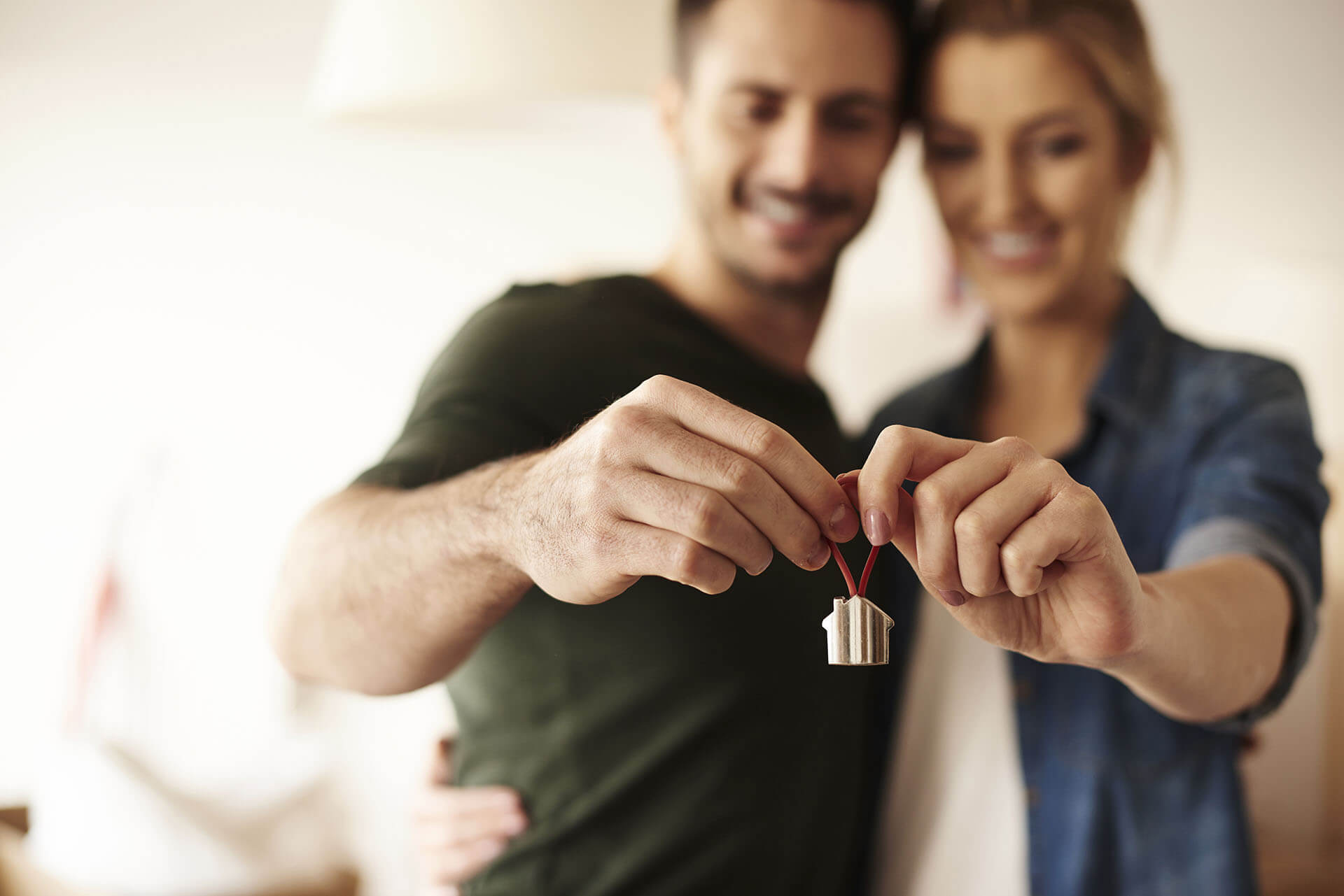 Couple smiling and holding a gold charm in the shape of a house signifying their home purchase